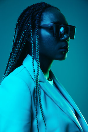 African american woman portrait business smile and fashion wearing glasses on blue background in neon light, color mixed light, bright color dancing, futuristic party. Flying pigtails hair emotions.の写真素材