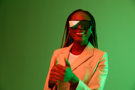 African american woman smile and fashion wearing glasses green background in neon light color mixed light, bright color dancing, futuristic party. Beauty African American woman with pigtails emotions.の写真素材