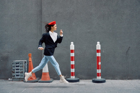 Fashion woman running down the street in front of the city tourist in stylish clothes with red lips and red beret, travel, cinematic color, retro vintage style, late to work.の写真素材