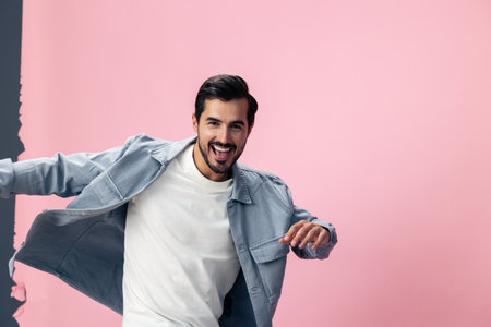 Stylish brunette man with beard happiness open mouth jumping and running spreading his arms on a pink background in a white T-shirt and jeans smile and joyful emotion on his face, copy spaceの写真素材