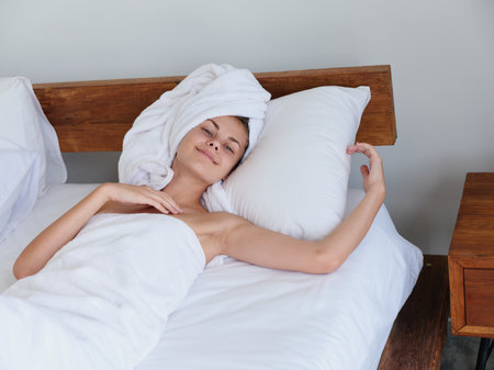 Woman lying on bed after shower with wet hair with towel on her head in bedroom, cute smile with teeth and weekend rest in bed, womens beauty day, healthy sleep, lifestyleの写真素材