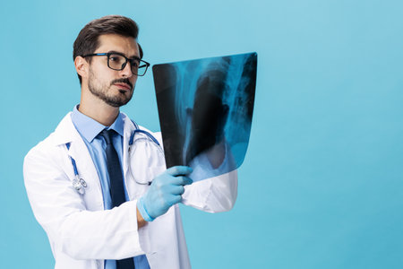 Male doctor in a white coat surgeon looks at an x-ray of a patient smile on a blue isolated background, copy space, space for textの写真素材