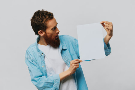 Portrait of an adult male on a gray background with a white sheet of paper in his hands for your design and text, layout, copy space, space for text, finger pointingの写真素材