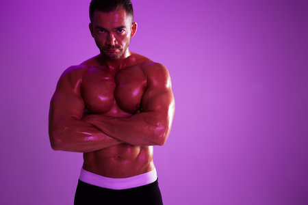 Man athletic body bodybuilder in briefs with nude torso abs full-length in the background fitness classes, purple colored light. Advertising, sports, active lifestyle, competition, challenge concept.の写真素材