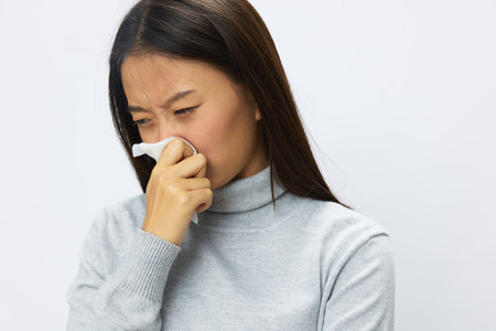 Asian woman holding hand with handkerchief and coughing up flu and cold, stuffy nose viral disease asthma and allergies covid, white backgroundの写真素材