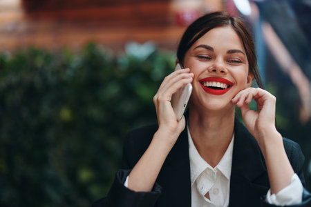 Woman blogger tourist sits in a cafe at a table with a phone in her hands conversation, mobile communication and internet in spring travel, video business call, freelance work online, smile with teethの写真素材