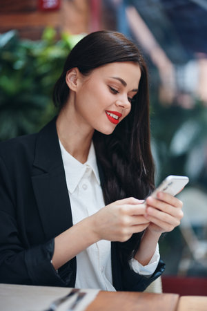Fashion woman blogger tourist sits in a cafe with a phone in her hands reads a message, mobile communication and internet in travel spring, video call, freelance work online, smile with teethの写真素材