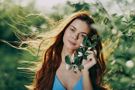 Beautiful woman smile close-up face with long red hair flying hair near the tree in the summer sun in the nature in the park smiling without allergies in a blue dress, the concept of health and beautyの写真素材