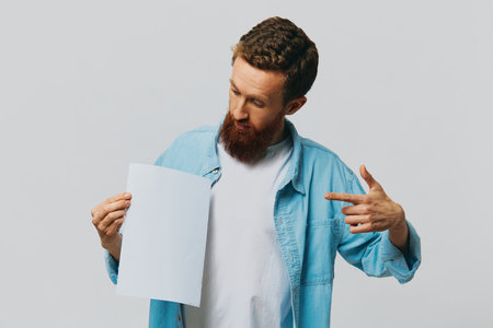 Portrait of an adult male on a gray background with a white sheet of paper in his hands for your design and text, layout, copy space, space for text, finger pointingの写真素材