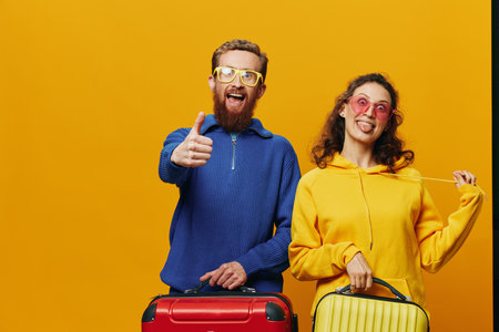 Woman and man smiling, suitcases in hand with yellow and red suitcase smiling merrily and crooked, yellow background, going on a trip, family vacation trip, newlyweds.の写真素材