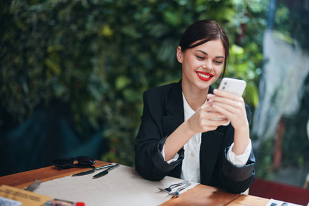 Fashion woman blogger tourist sits in a cafe with a phone in her hands reads a message, mobile communication and the Internet on a spring trip, video call, freelance work online, smile, communicationの写真素材