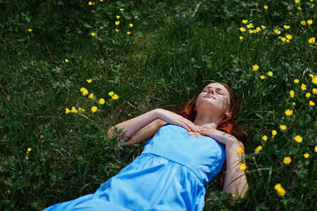Woman smile lies on the green grass in spring under the sun with yellow flowers, happiness, red long hairの写真素材