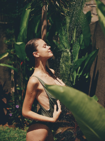 Sexy woman, body in a swimsuit takes a tropical shower outdoors against the backdrop of green...