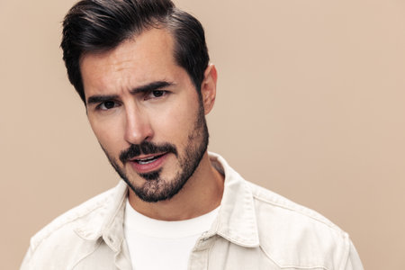 Portrait of a stylish man dissatisfied and angry screaming on a beige background in a white t-shirt looking at the camera, fashionable clothing style, copy space, space for textの写真素材