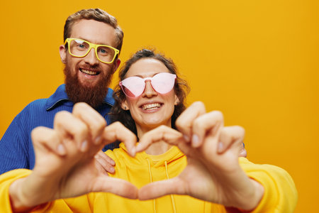 Man and woman couple smiling cheerfully and crooked with glasses, on yellow background, symbols signs and hand gestures, family shoot, newlyweds.の写真素材