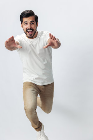 Fashion man jumping and running in a white t-shirt and jeans, smile with teeth joy on a white isolated background, fashionable clothing style, copy space, space for textの写真素材