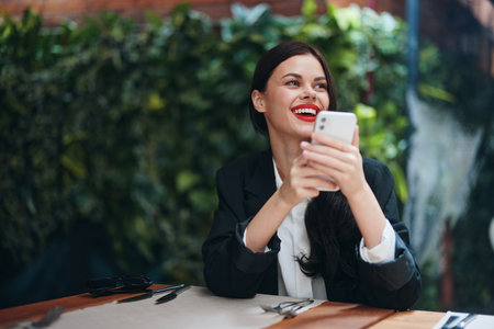 Fashion woman blogger tourist sits in a cafe with a phone in her hands reads a message, mobile communication and internet in travel spring, video call, freelance work online, smile with teethの写真素材