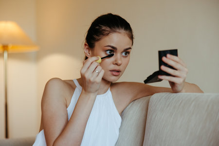 A woman at home looks in the mirror and apply makeup dye mascara eyelashes, beauty concept, care for problem skin with acne.の写真素材