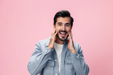 Portrait of a stylish brunette man with a beard beautiful smile on a pink background in a white T-shirt and jeans smile and joyful emotion on his face, copy spaceの写真素材
