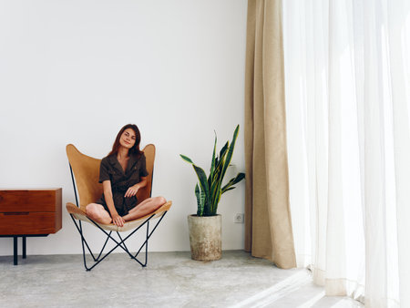 Woman sitting in a leather armchair near the window smiling , modern stylish interior Scandinavian lifestyle, copy space.の写真素材