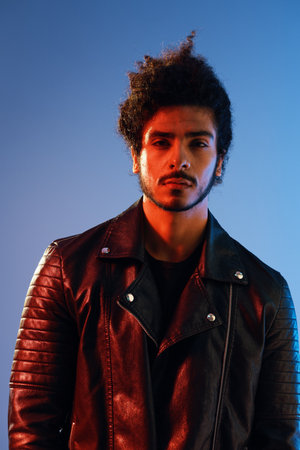 Portrait of a stylish man with curly hair on a blue background multinational, colored light, black...