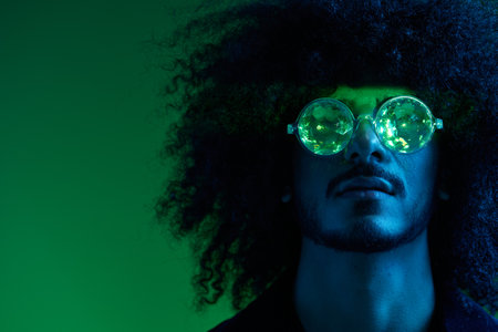 Fashion portrait of a man with curly hair on a green background with sunglasses, multinational, colored pink light, trendy, modern concept.の写真素材