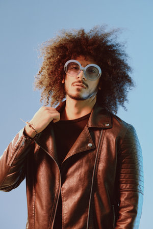 Portrait of a stylish man with curly hair with glasses smile on blue background multinational, color...