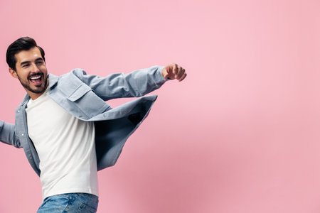 Stylish brunette man with beard happiness open mouth jumping and running spreading his arms on a pink background in a white T-shirt and jeans smile and joyful emotion on his face, copy spaceの写真素材