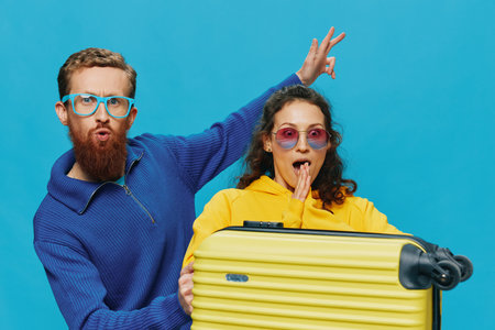 Woman and man smile sitting on suitcase with yellow suitcase smile, on blue background, packing for trip, family vacation trip.の写真素材
