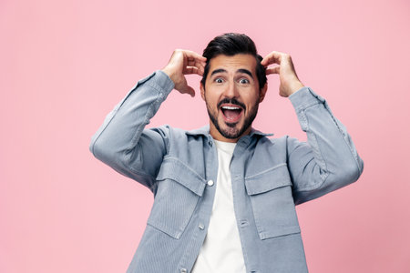 Portrait of a stylish brunette man with a beard raised his hands up with surprise open pink background in a white T-shirt and jeans smile and joyful emotion on his face, copy spaceの写真素材