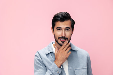 Fashion portrait of a brunette man with a beard on a pink background in a white T-shirt with a smile and joyful emotion on his face, copy spaceの写真素材