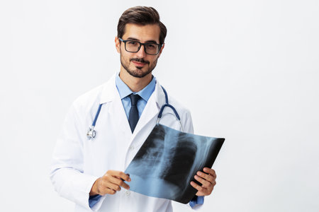 Man doctor in white coat and eyeglasses and stethoscope with a smile looks at patient X-ray images...