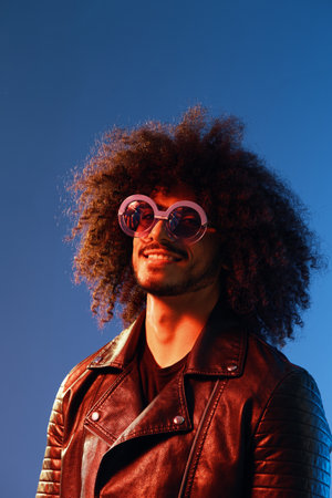 Portrait of a stylish man with curly hair with glasses smile on blue background multinational, color...