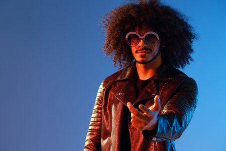 Portrait of a stylish man with curly hair with glasses smile on blue background multinational, color light, black leather jacket trend, modern concept.の写真素材