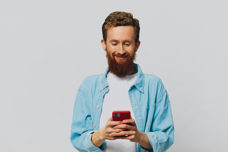 Man hipster with phone in hand blogger smile on gray background in blue shirt and white t-shirt, talking on the phone and selfiesの写真素材