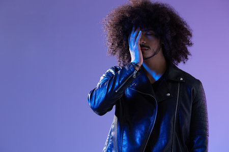 Portrait of fashion man with curly hair on blue background multinational, colored light, black...