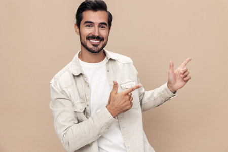 Portrait of a stylish man smile with teeth and surprise raised his hands up on a beige background in a white t-shirt, fashionable clothing style, copy space, space for textの写真素材