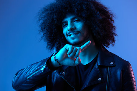 Portrait of fashion man with curly hair on blue background multinational, colored light, black...
