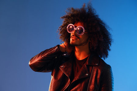 Portrait of a stylish man with curly hair with glasses smile on blue background multinational, color...