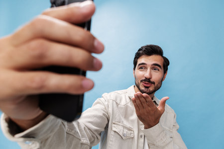 Portrait of a man brunette smile looking at the phone blogger with a beard taking selfies, on a blue...