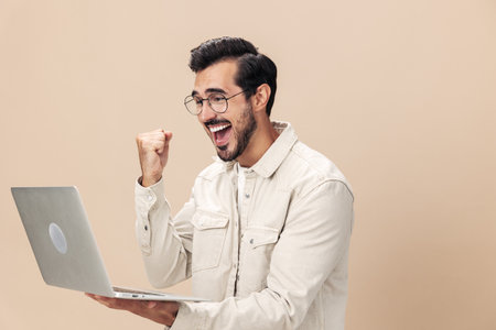 Portrait of a stylish with a laptop in his hands mockup, working freelancer smile with teeth open mouth slavery victory, beige background in a white t-shirt, fashionable clothing style, space spaceの写真素材