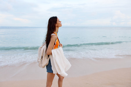 A young woman after swimming in the ocean with a backpack in wet clothes walks along the beach, summer vacation on an island near the ocean in Baliの写真素材