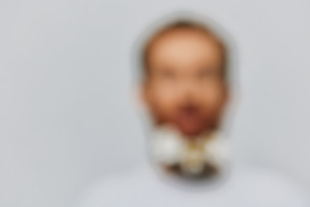 Portrait of a funny man in a white T-shirt with flowers daisies in his beard on a white isolated background, copy place. Holiday concept and congratulations.の写真素材