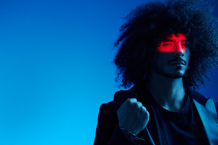 Fashion portrait of a man with curly hair on a blue background, multinational, colored light, trendy, modern concept.の写真素材