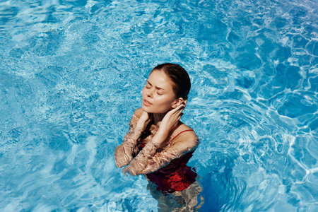 Happy woman swimming in the pool in red swimsuit with loose long hair in the sunshine, skin...
