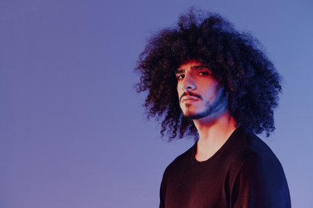 Portrait of a stylish man with curly hair in smoke on a blue background multinational, color light,...