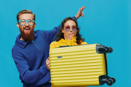 Woman and man smile sitting on suitcase with yellow suitcase smile, on blue background, packing for trip, family vacation trip.の写真素材