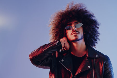 Portrait of a stylish man with curly hair on a blue background multinational, colored light, trendy glasses, modern concept.の写真素材