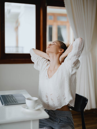 Creative young woman working at a desk at home in a cozy interior with a cup of drink, home office...