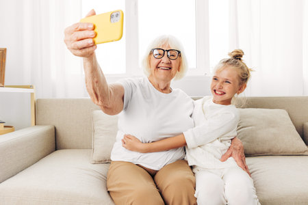 Grandmother sofa smiling granddaughter child selfie family togetherness phone bonding huggingの写真素材